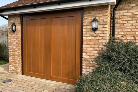 A wood-tone automated up-and-over GRP garage door with elegant paneling and a natural finish.